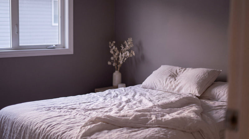 Early morning light falling across white linen bedding in a quiet, dim bedroom