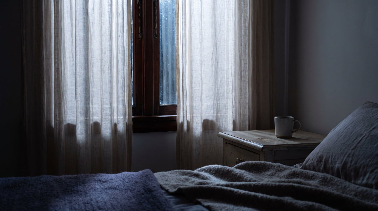 Moonlight filtering through sheer linen curtains at a bedroom window at night